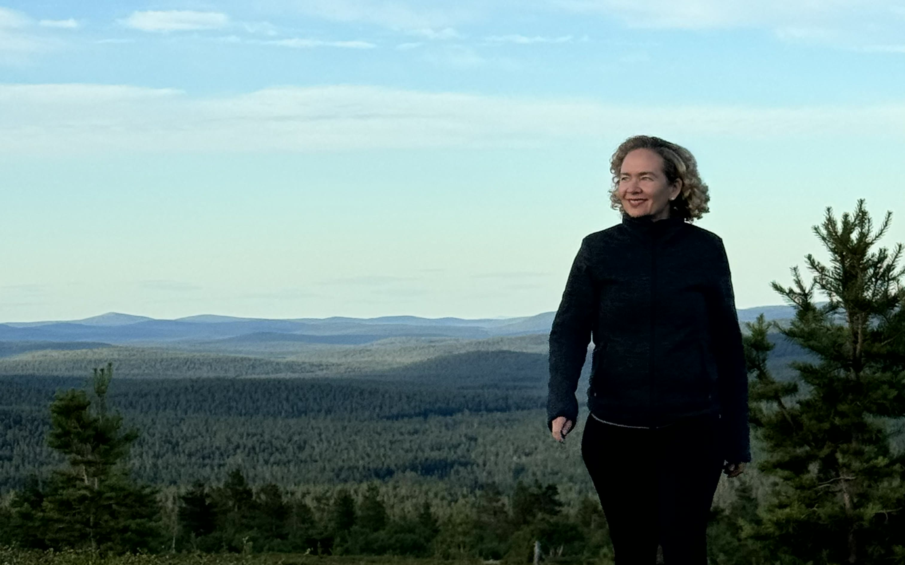 Tarja Stephens standing on a Lapland fell, forest and hills behind her