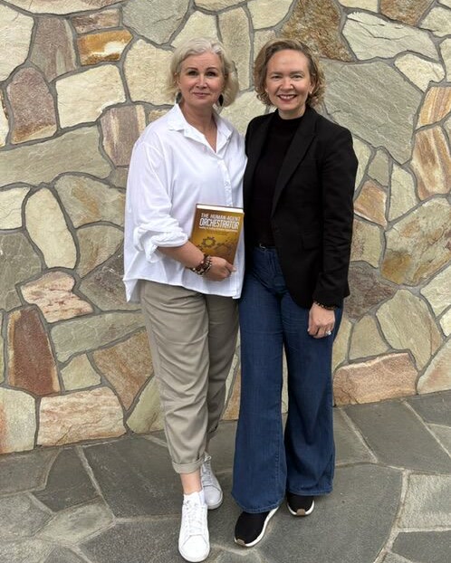 Tarja and a reader with the book in front of a stone wall.