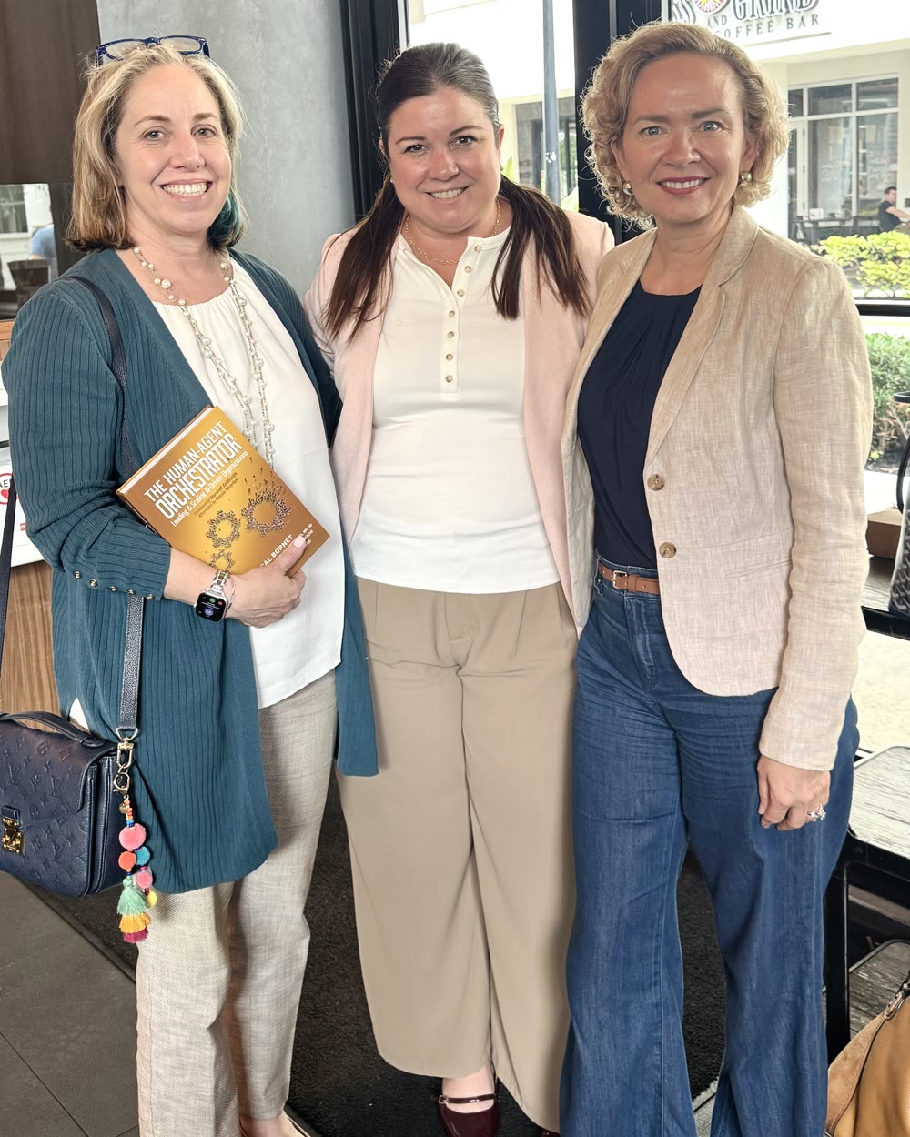 Three women holding The Human-Agent Orchestrator at a leadership event.